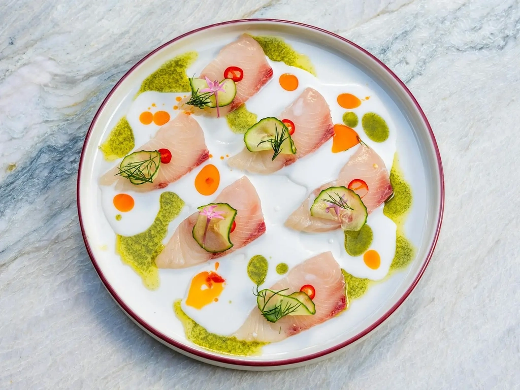 Kingfish crudo with cucumber, dill, chilli and herb oil on a white plate