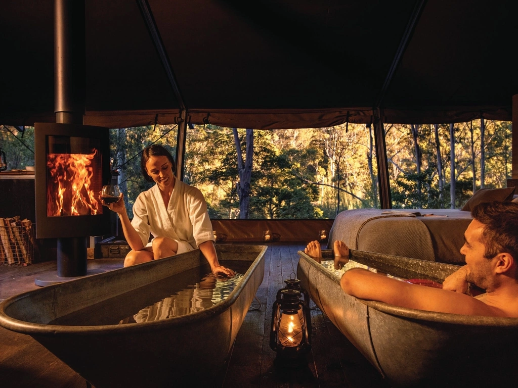Couple enjoying bath by the fire inside safari tent with view to the natural environment.