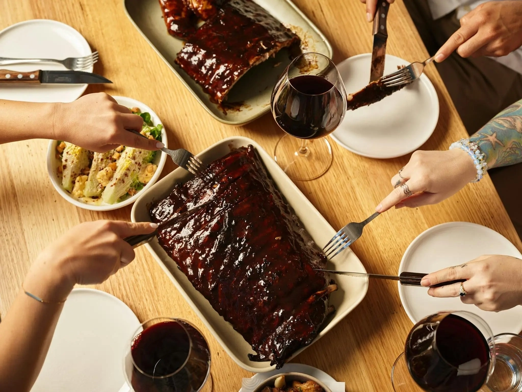 Delicious racks of Hurricane's flame-grilled pork ribs being cut into with knives and forks.