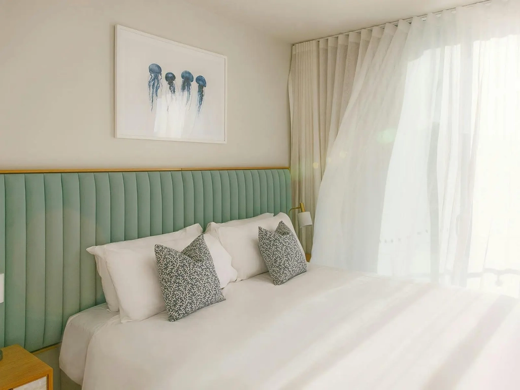 Bright Kirra Point bedroom with king bed, coastal artwork, and sheer curtains flowing in light.
