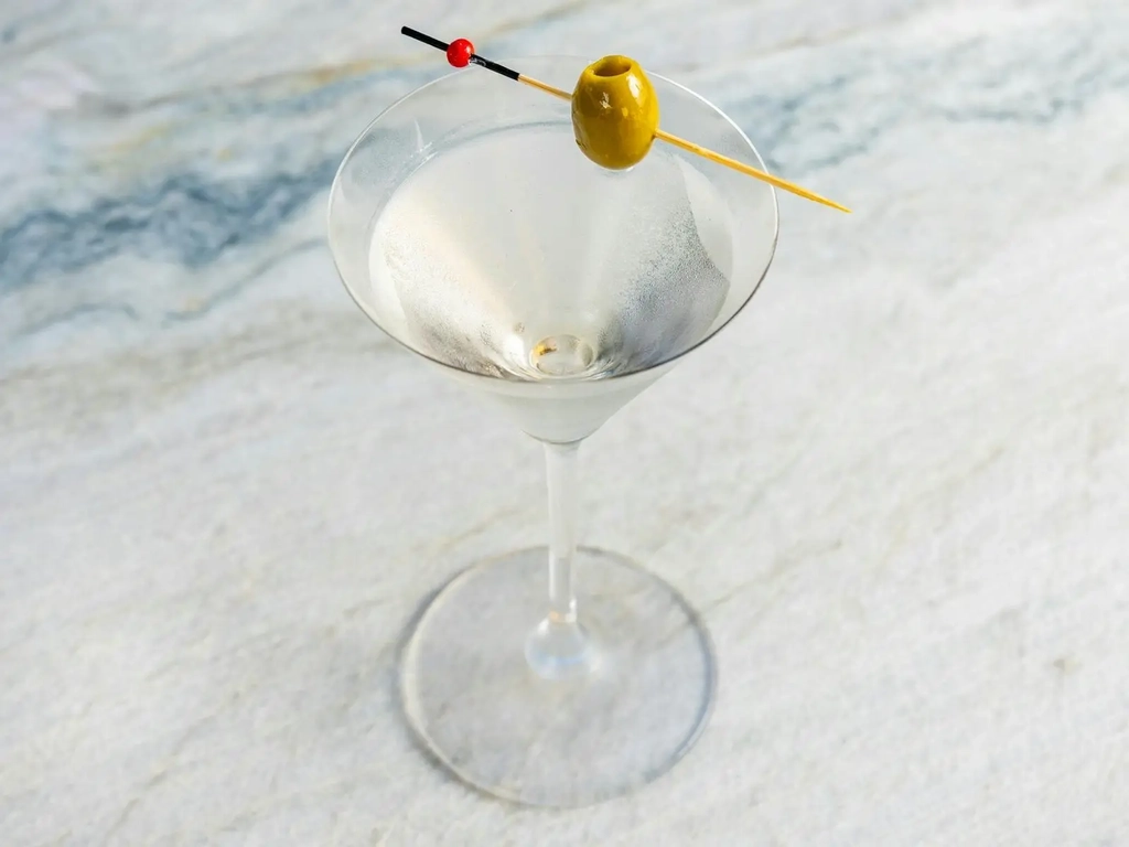 Classic martini with a green olive on a marble bar