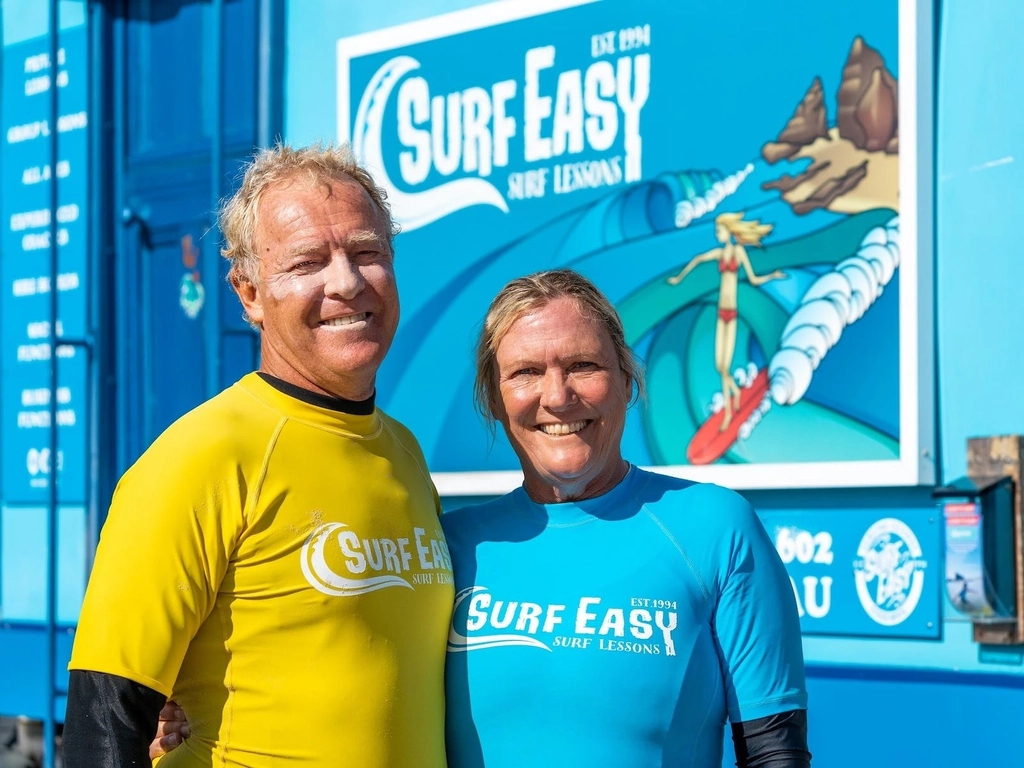 Man and woman smiling in front of surf school van.