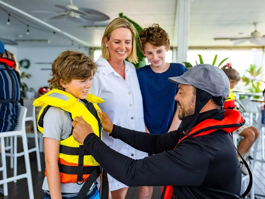 Jet boat pilot assisting a child to put on a life jacket.