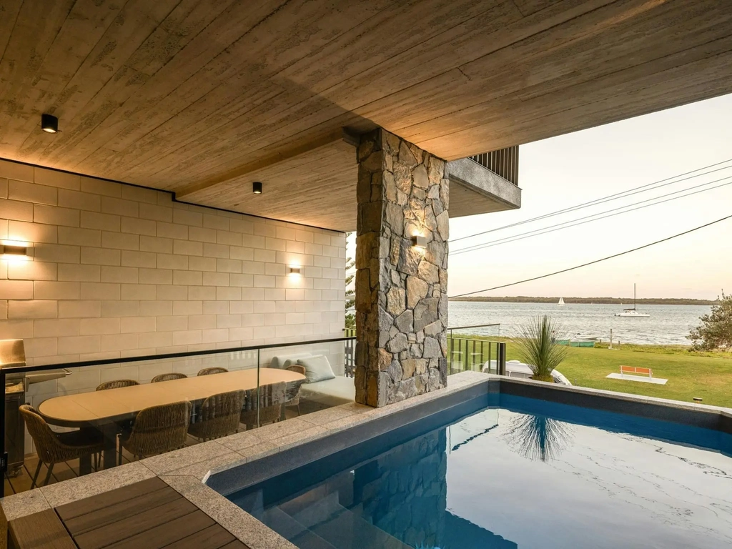 Covered waterfront terrace with a heated spa and a long dining table
