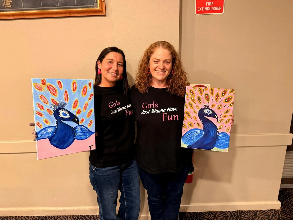 Two Paint Juicy guests smiling with their finished peacock artwork