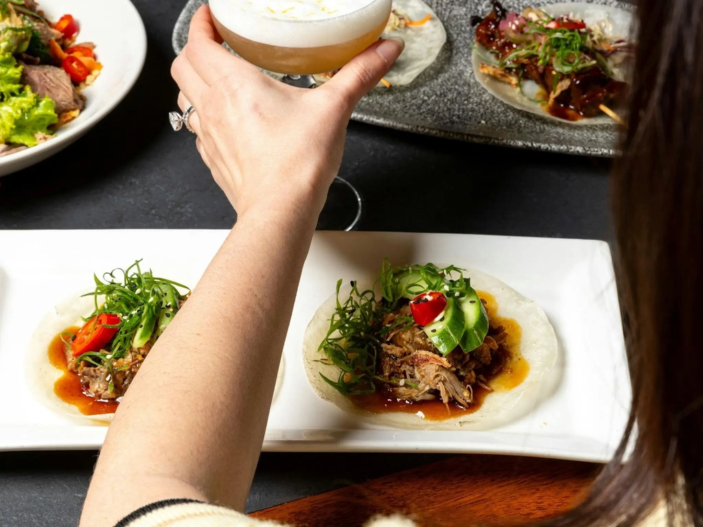 Asian fusion food spread with person holding cocktail