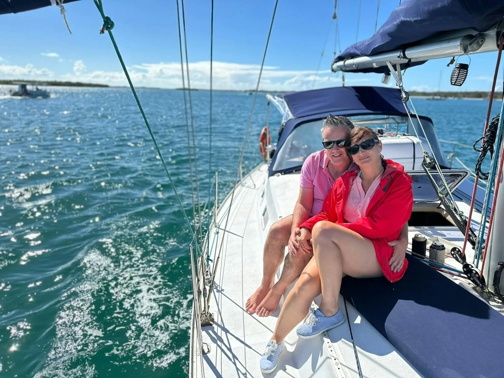 Lady in red and man in pink sitting on the deck of Sun Sailing's yacht during a sunset shared cruise