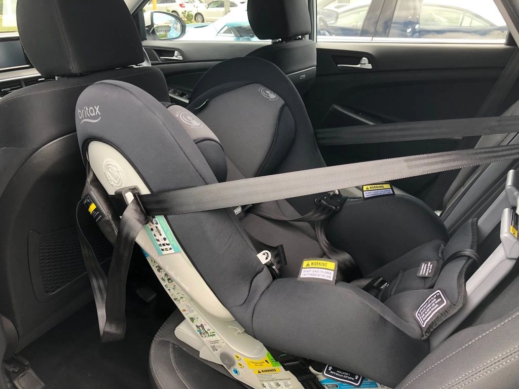 A greay rearward facing car seat installed into a car.