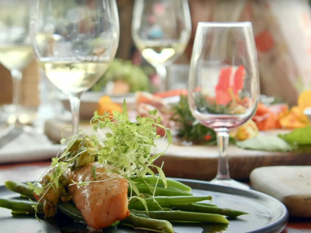 A plate of salmon with green beans and potatoes with glasses of wine on the table