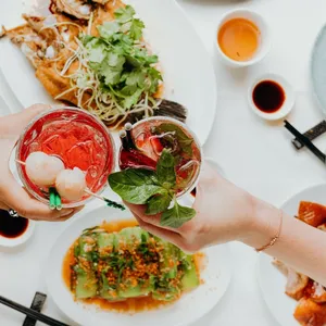 Two people hold two drinks above a spread of food.