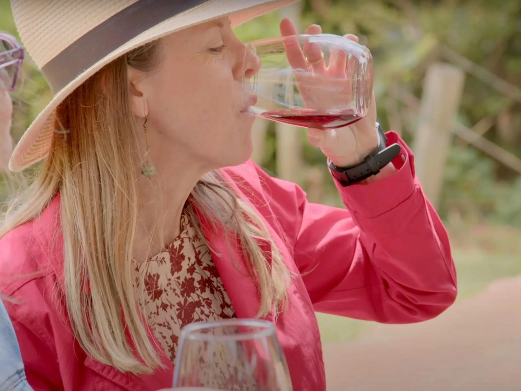 A women wearing a red jacket and straw hat sipping a glass of red wine at Witches Fall Winery