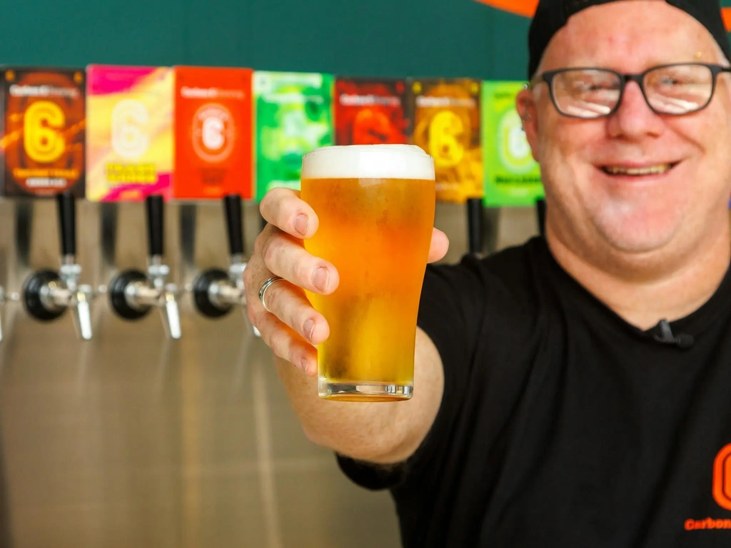 A man behind the bar handing a glass of freshly poured craft beer