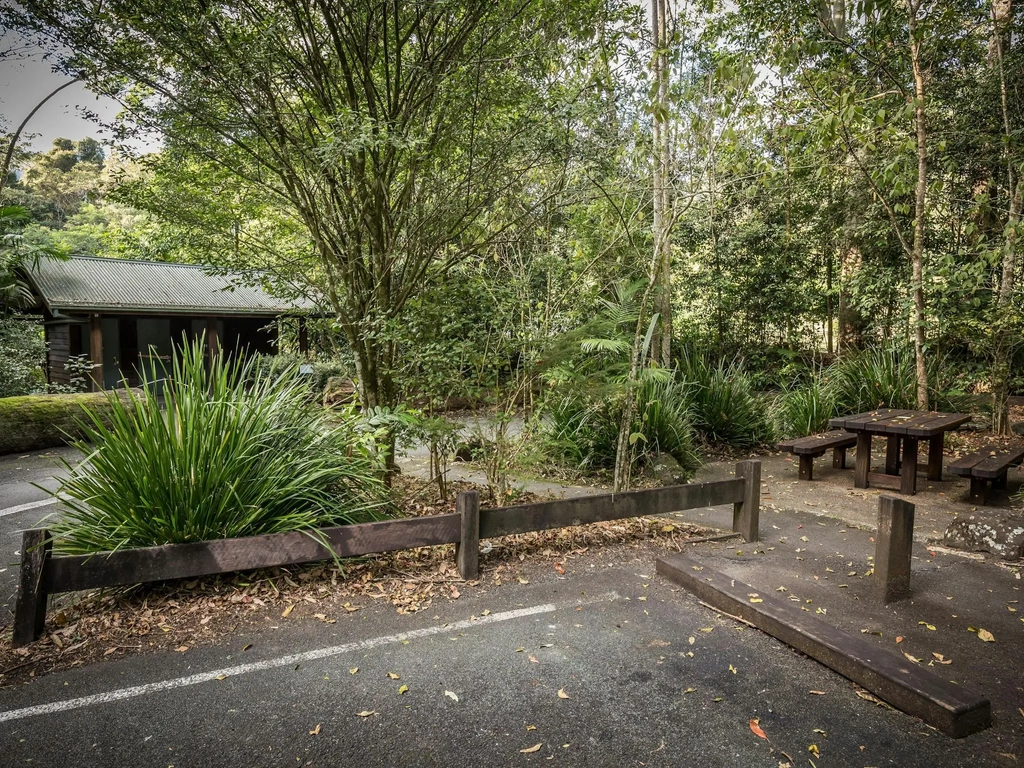 Toilets in the background, wooden picnic table on the right and a car park in the foreground.