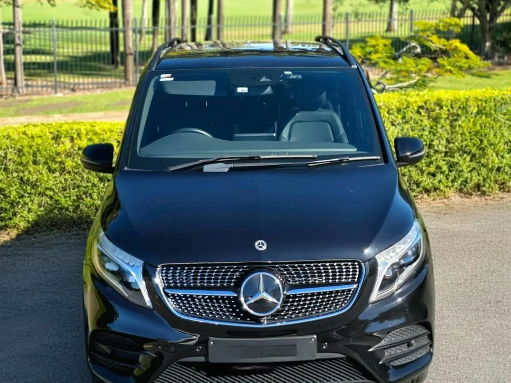 Front view of a black Mercedes-Benz van with golf course scenery and trees in the background.