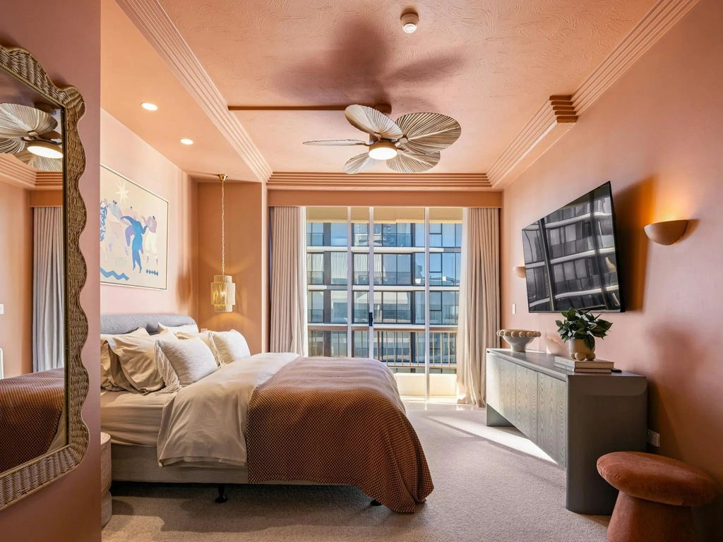 Main bedroom with a king bed, dusty terracotta pink walls and a ceiling fan