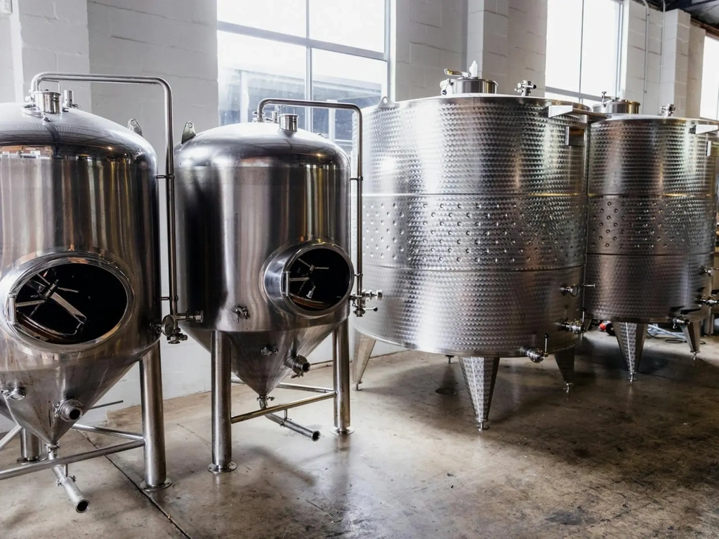 Distilling equipment, including copper stills and tanks, set up in a distillery environment.