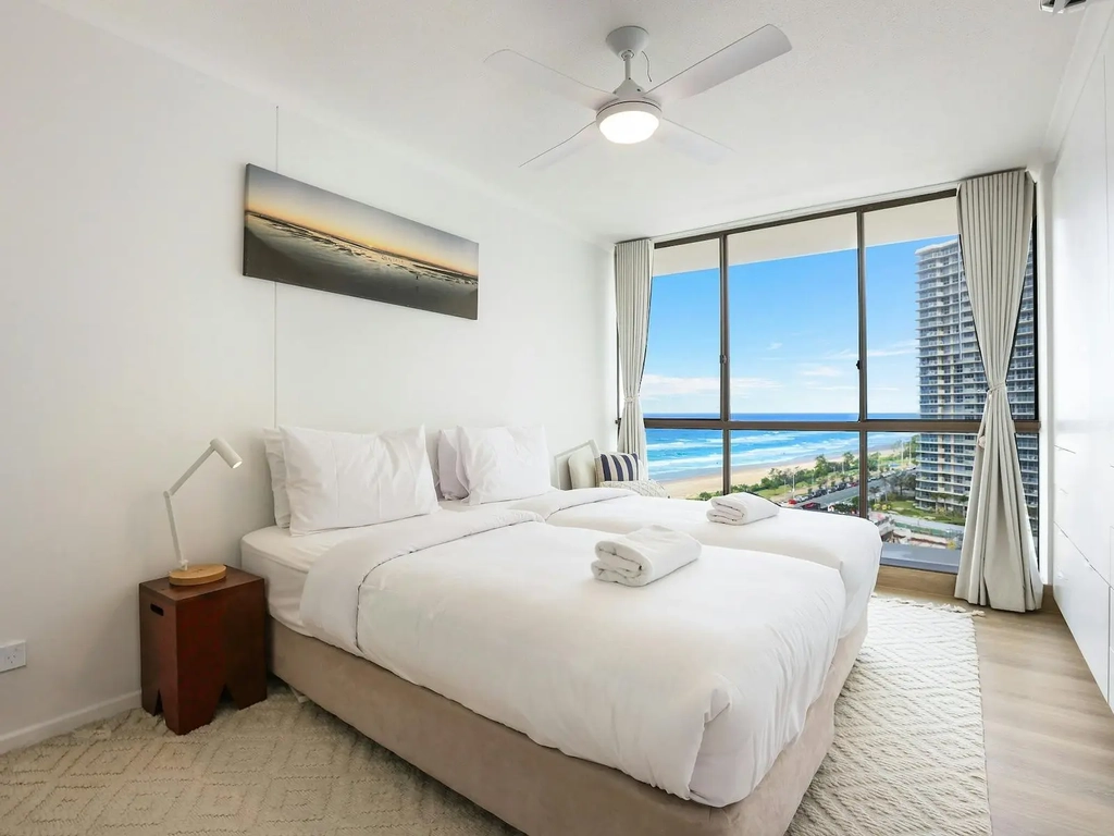 Second bedroom with 2 single beds with floor to ceiling windows on the left side with ocean/ city