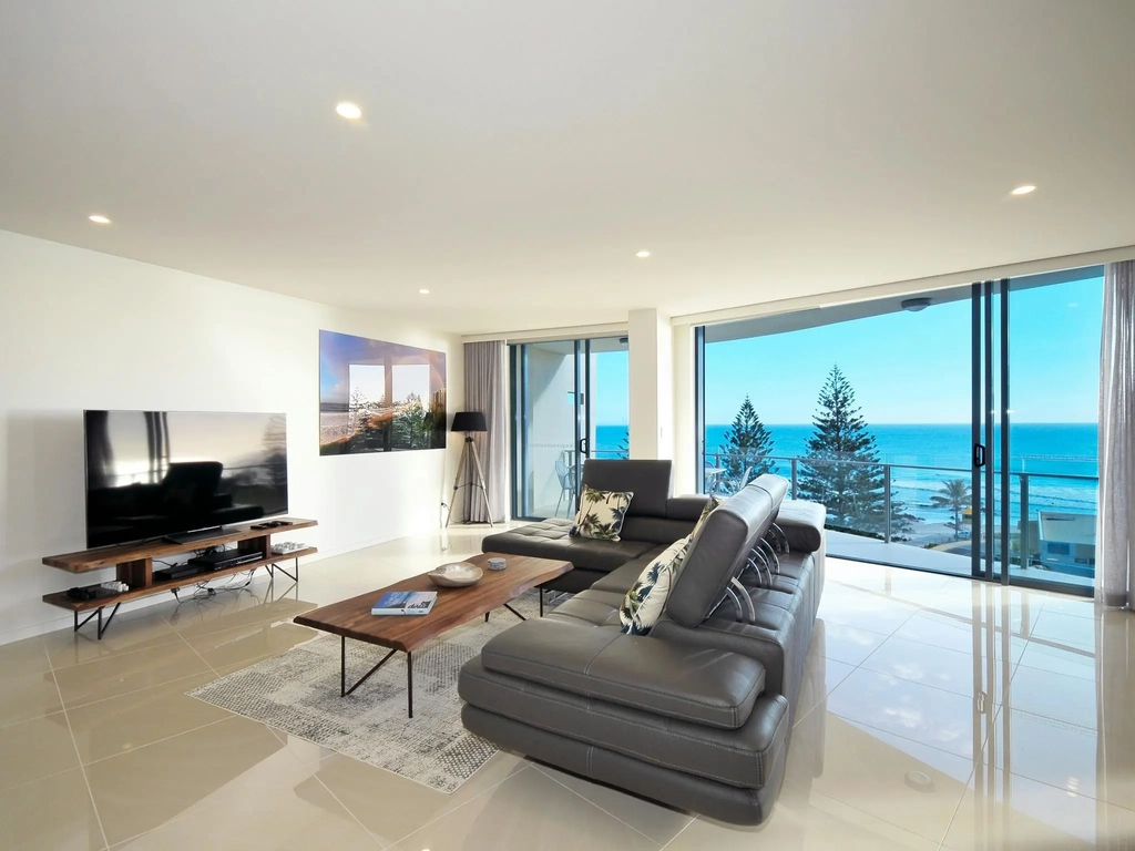 Contemporary lounge with high-gloss neutral tiles, brown leather sofa, and breathtaking ocean views