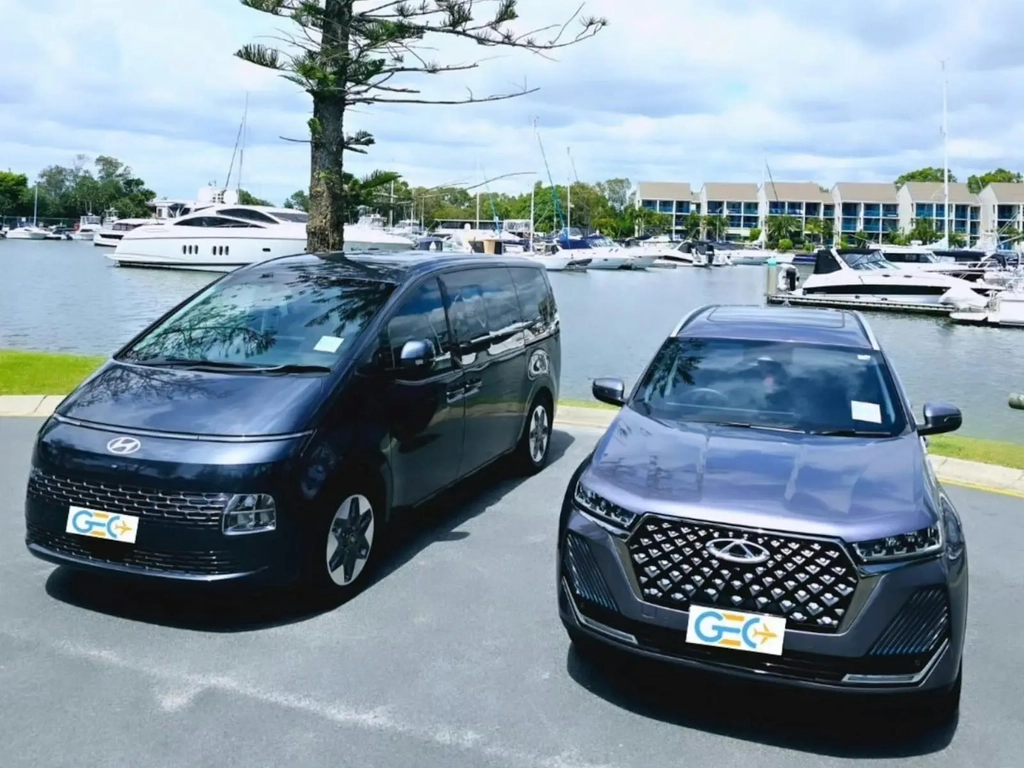 Hyundai van and Chery SUV from GEC Transfers parked near a marina with yachts and waterfront