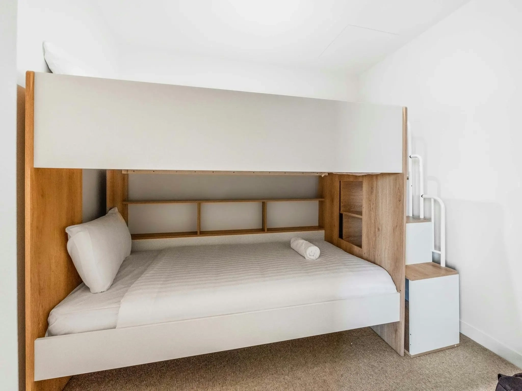 Bunk room with a wider lower bed and timber steps instead of a ladder.