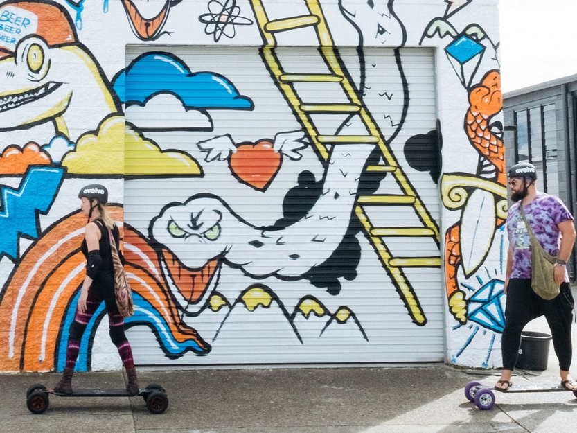 Skaters rolling past the Precinct mural