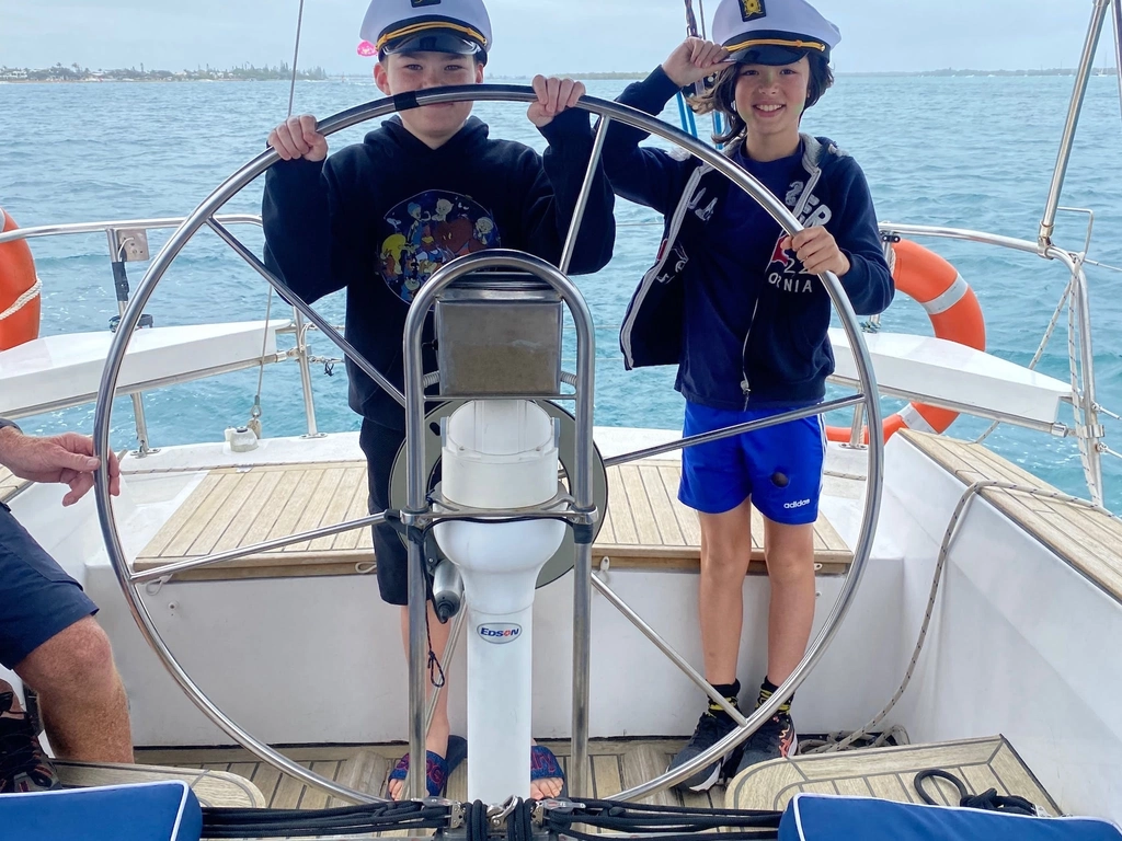 Two children with captains hats on steering the yacht on Sun Sailing's midday shared cruise