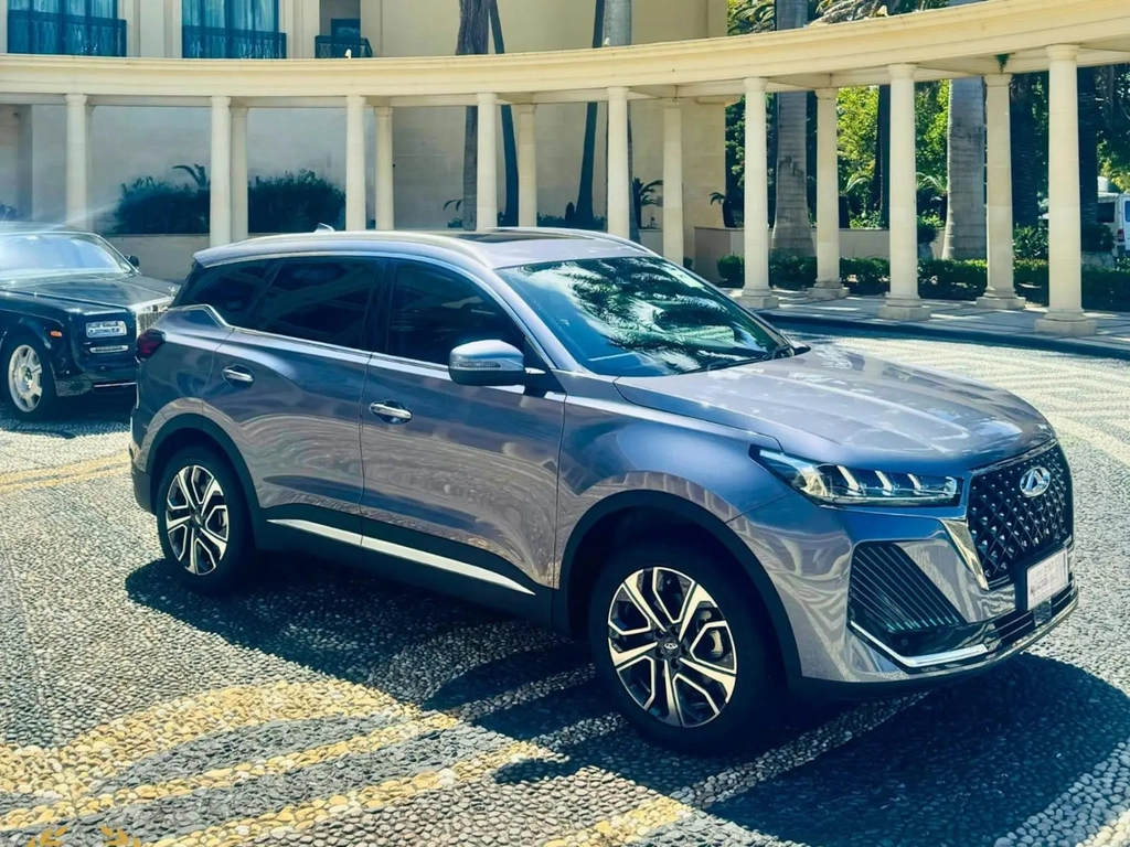 Sleek grey Chery SUV parked in front of a luxury hotel with palm trees and architectural columns.