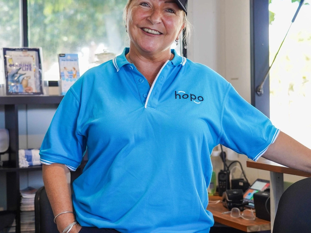 Woman in Hopo blue polo shirt smiles at camera inside Hopo Information Kiosk