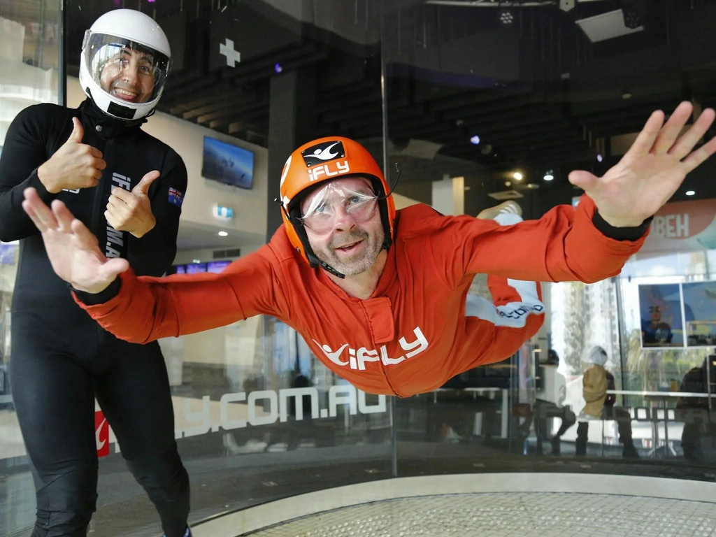 Intstructor gives a thumbs up to the camera while male in an orange suit flies solo.