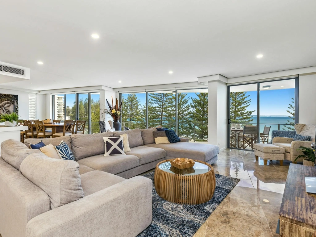 Cozy lounge with warm tones, grey corner sofa, marble tiles, and beautiful ocean views